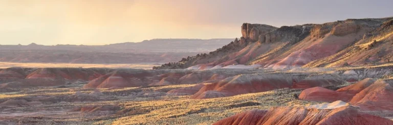 Wijds woestijnlandschap van de Painted Desert met een rotsformatie in de verte tijdens een gloeiende zonsondergang