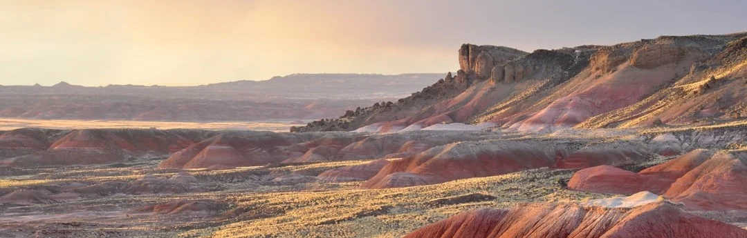 Wijds woestijnlandschap van de Painted Desert met een rotsformatie in de verte tijdens een gloeiende zonsondergang