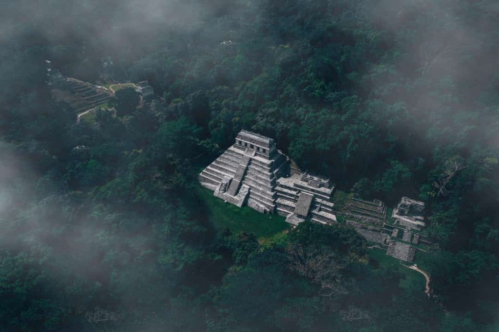 Luchtfoto van een stenen Mayapiramide die tussen dichte jungle en optrekkende mist uitsteekt bij Palenque