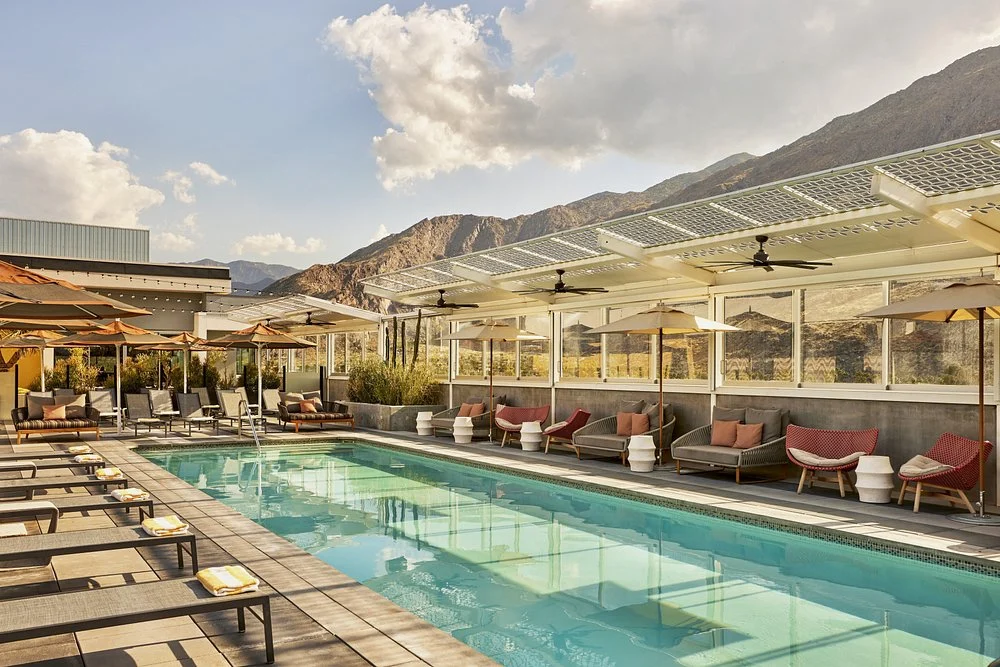 Lang zwembad op een dakterras met loungebanken en parasols en uitzicht op kale bergtoppen bij zonsondergang in Palm Springs