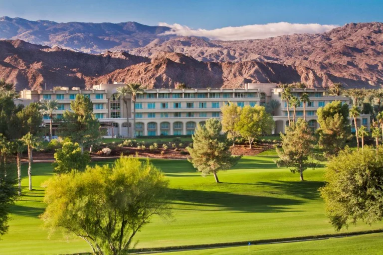 Hotelcomplex met palmbomen en een golfbaan op de voorgrond, met kale bergen op de achtergrond in Palm Springs
