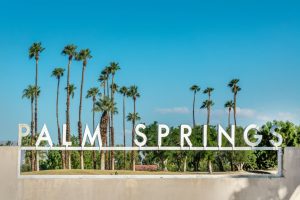 Groot wit bord met de tekst Palm Springs, omringd door hoge palmbomen tegen een strakblauwe lucht