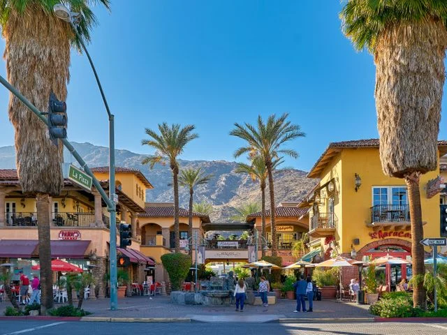Kleurrijke gebouwen met terrassen en hoge palmbomen op een plein met op de achtergrond de bergen rond Palm Springs