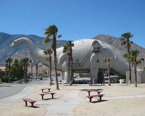 Enorm dinosaurusbeeld tussen palmbomen langs de weg bij de bezienswaardigheid van Cabazon in Californië