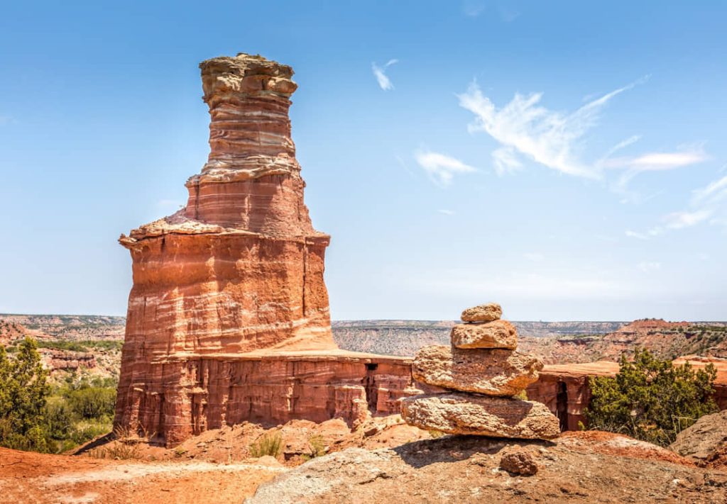 Hoge zuilvormige rode rotsformatie bekend als The Lighthouse, met een gestapelde steenformatie op de voorgrond in Palo Duro Canyon in Texas