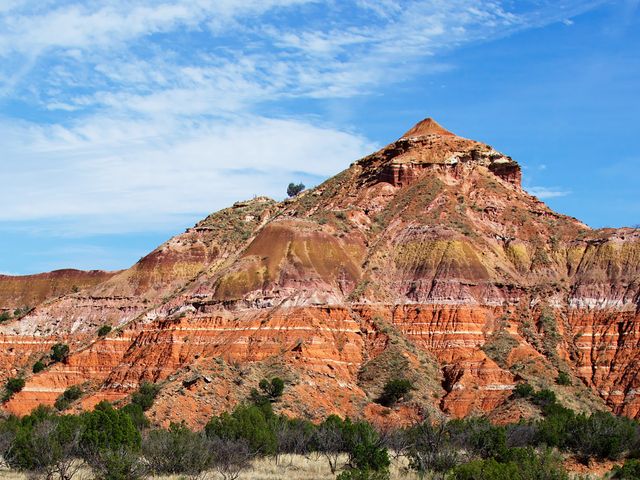 Piramidevormige heuvel met rode, gele en roestkleurige gesteentelagen in Palo Duro Canyon onder een blauwe lucht