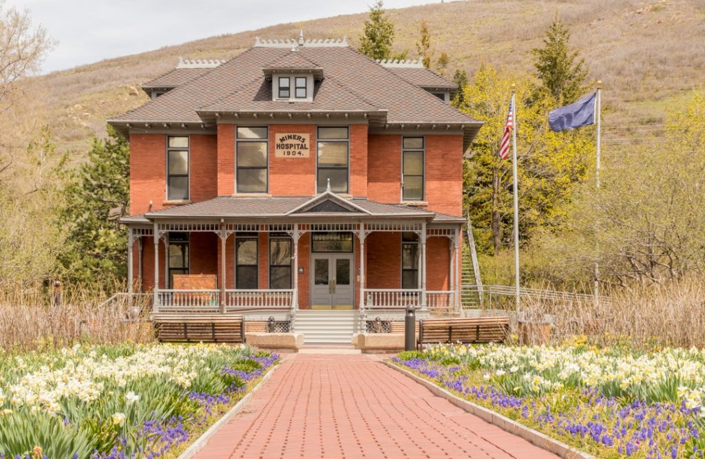 Rood bakstenen gebouw uit 1904 van het voormalige Miners Hospital in Park City met een bakstenen pad tussen bloemperken
