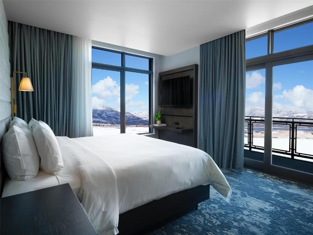 Hotelkamer met een groot wit bed en een balkon met uitzicht op besneeuwde bergen
