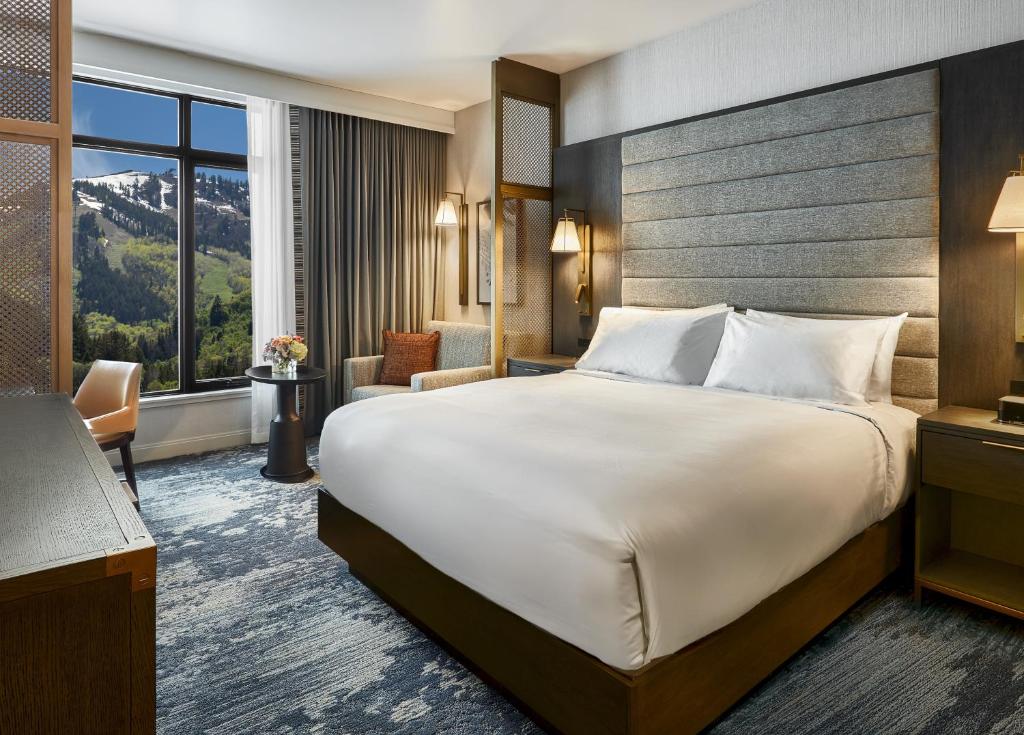 Hotelkamer met een groot bed en een raam met uitzicht op een besneeuwde skipiste tegen de bergen
