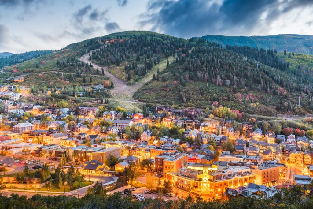 Luchtfoto van het verlichte centrum van Park City tegen een beboste berghelling bij schemering