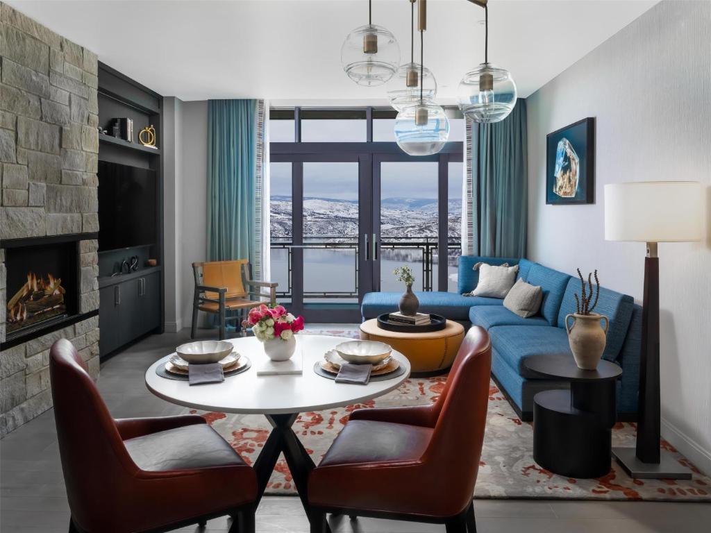 Ruime woonkamer van een hotelsuite met een openhaard, blauwe bank en een eettafel met uitzicht op een meer