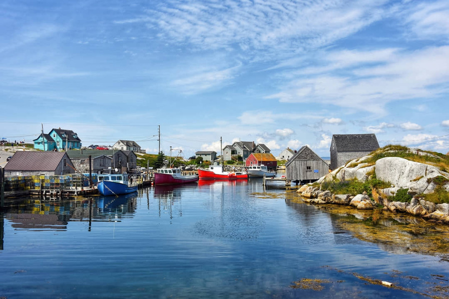 Rode en blauwe vissersboten liggen afgemeerd in de kleine haven van Peggy's Cove tussen houten vissershutjes en rotsen