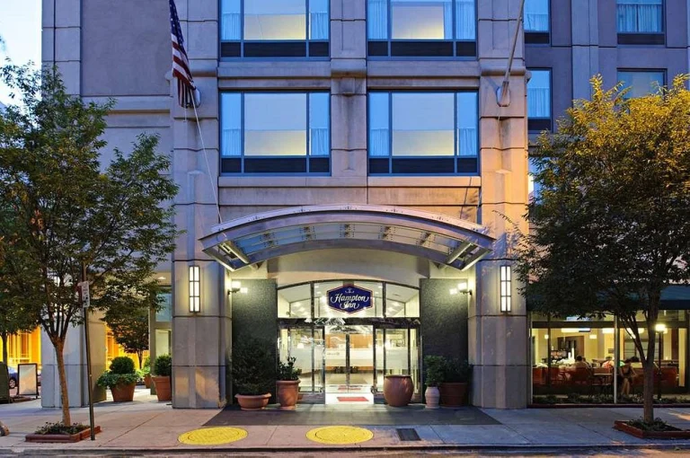 Verlichte entree van een Hampton Inn hotel in een hoog stenen gebouw met een Amerikaanse vlag in een stad