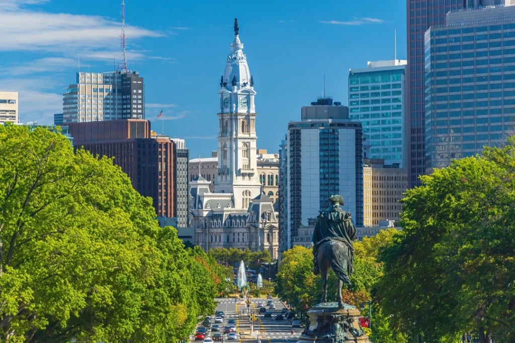Uitzicht op de klokkentoren van City Hall in Philadelphia langs een boulevard met bomen en een ruiterstandbeeld op de voorgrond