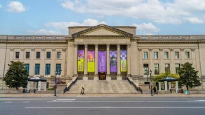 Zuilengevel van The Franklin Institute met kleurrijke banieren tussen de pilaren en voorbijgangers op straat
