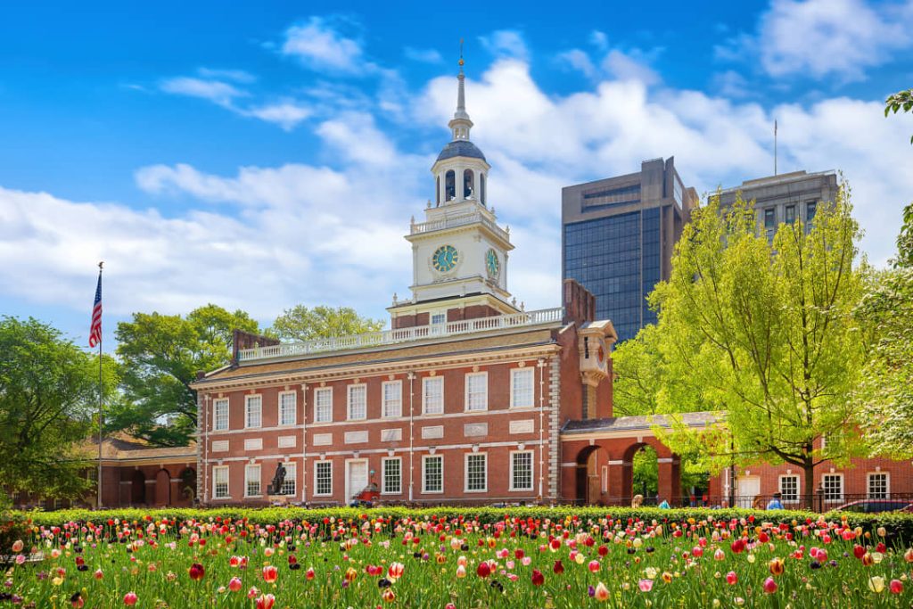 Bakstenen gevel en klokkentoren van Independence Hall met een kleurrijk bloembed vol tulpen op de voorgrond onder een blauwe lucht