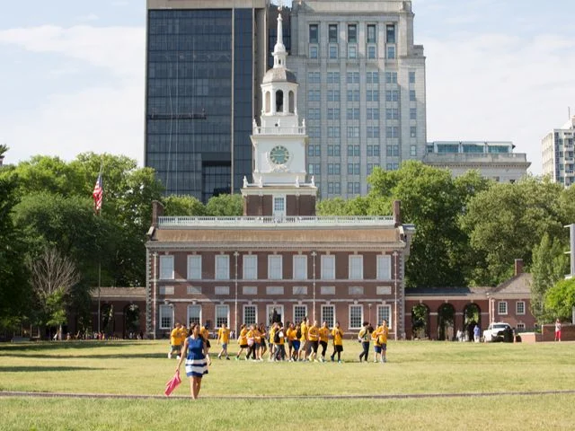 Rood bakstenen gebouw van Independence Hall met een klokkentoren in Philadelphia terwijl een groep mensen in gele shirts over het gazon loopt