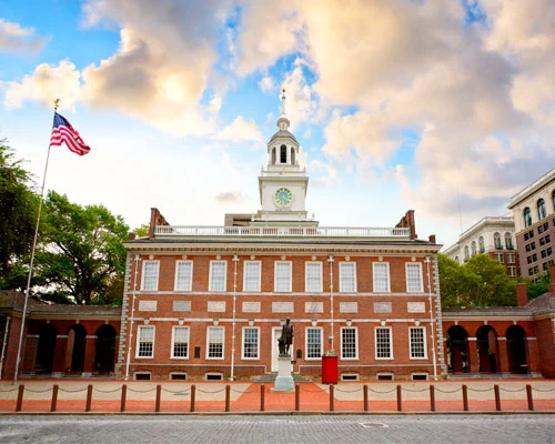 Bakstenen gebouw van Independence Hall in Philadelphia met een witte klokkentoren, Amerikaanse vlag en een standbeeld op het voorplein