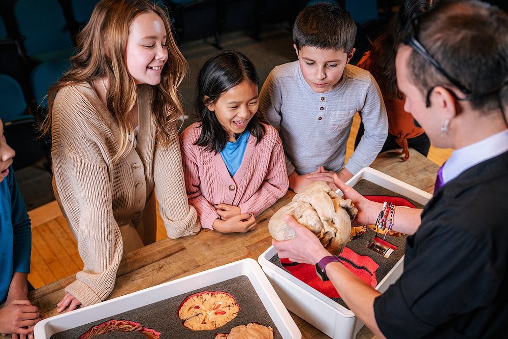 Groep kinderen kijkt geboeid naar een gids die fossielen en botten uit een dienblad laat zien