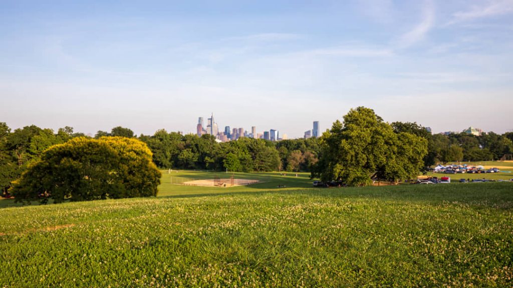 Uitzicht over een grasveld met bomen naar de verre wolkenkrabbers van het centrum van Philadelphia onder een blauwe lucht