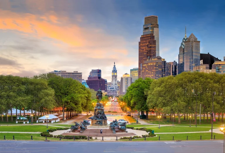 Standbeeld en fontein op Eakins Oval met uitzicht over de Benjamin Franklin Parkway naar de verlichte wolkenkrabbers van Philadelphia bij zonsondergang