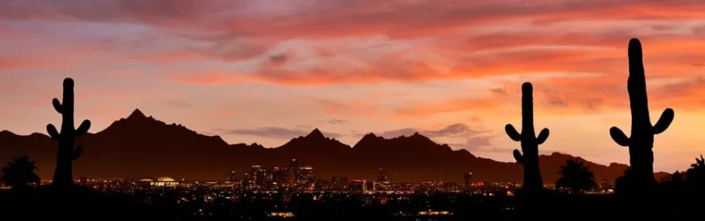 Silhouetten van saguaro cactussen en bergen tegen een felrode avondlucht boven de skyline van Phoenix in Arizona