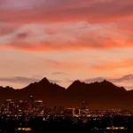 Silhouetten van saguaro cactussen en bergen tegen een felrode avondlucht boven de skyline van Phoenix in Arizona