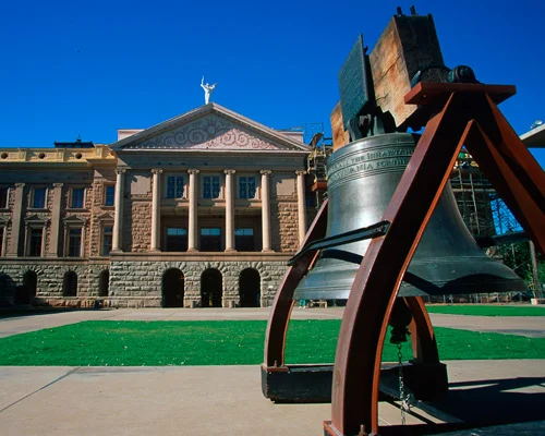 Klassiek gebouw met zuilen van het Arizona State Capitol met op de voorgrond een grote bronzen replica van de Liberty Bell