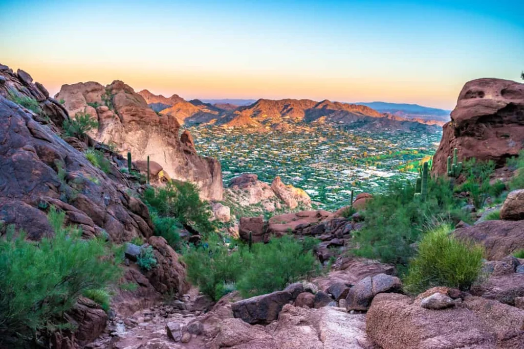 Rotsachtig pad tussen cactussen leidt naar een uitzicht over de stad Phoenix met bergen op de achtergrond bij zonsopgang