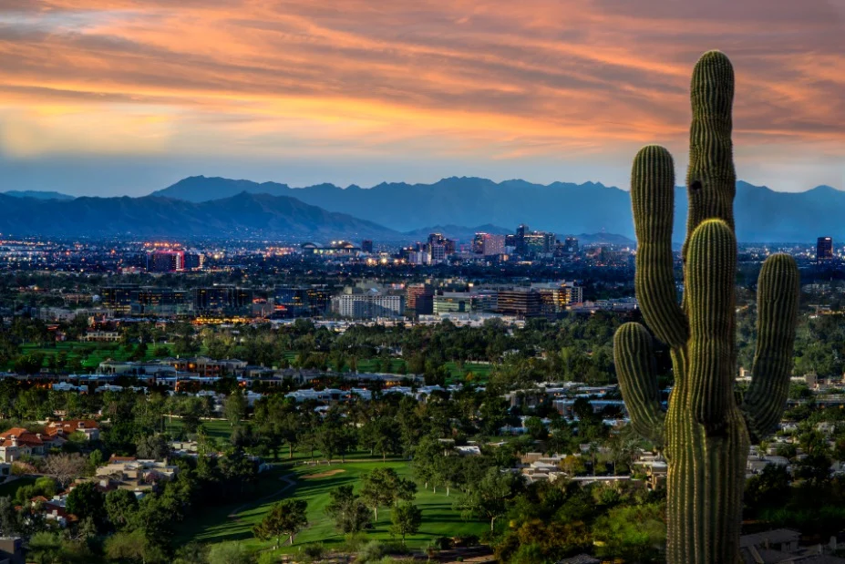 Uitzicht over de skyline van Phoenix bij een kleurrijke avondlucht met een grote saguarocactus op de voorgrond en bergen in de verte
