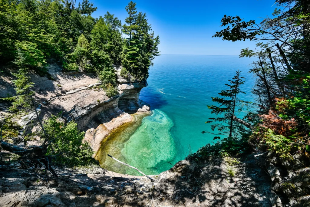 Uitzicht van bovenaf op een klein turquoise baaitje omringd door zandsteenkliffen en bos bij Pictured Rocks National Lakeshore in Michigan