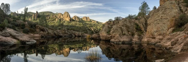 Ruige rotsformaties en begroeide heuvels van Pinnacles National Park weerspiegeld in het rustige water van een meer