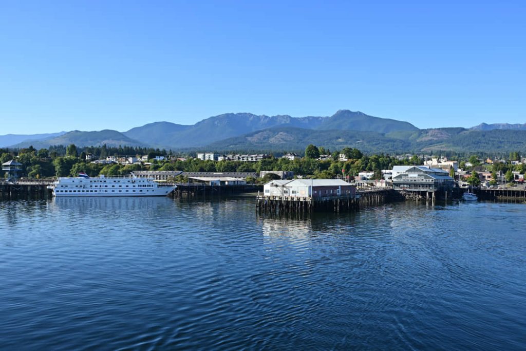Kleine havenstad met een witte veerboot aangemeerd bij een pier, gebouwen aan het water en besneeuwde bergen op de achtergrond in Washington