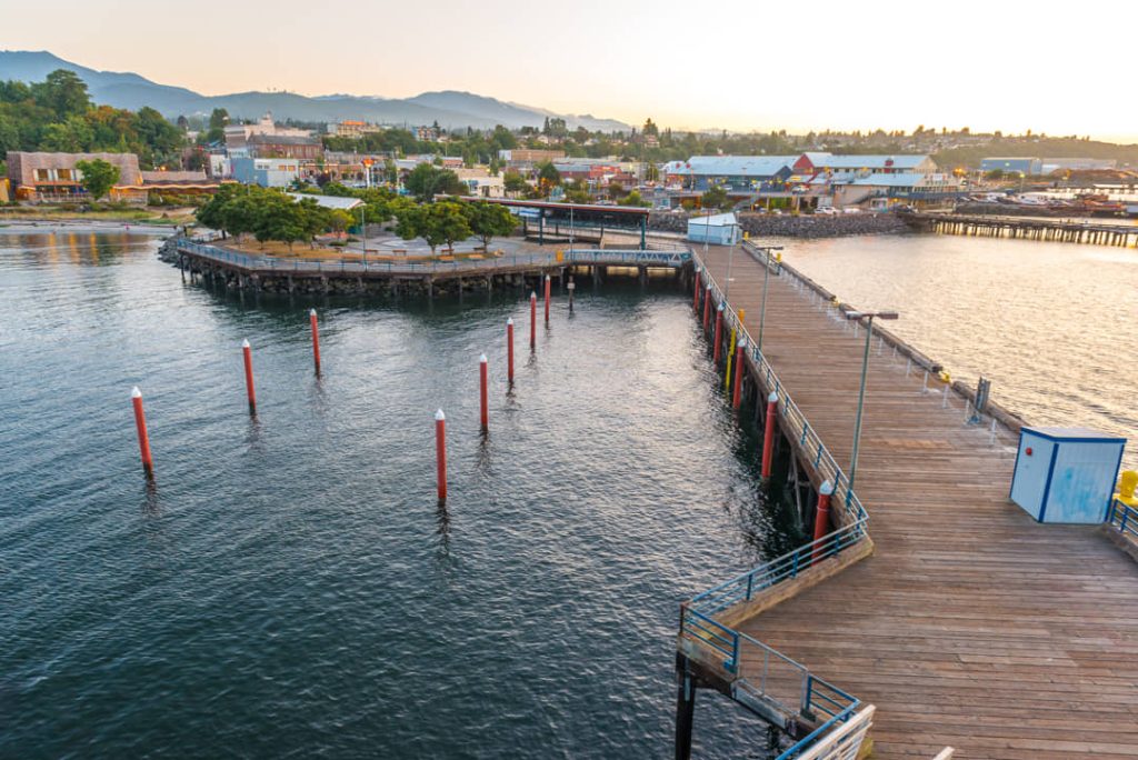 Luchtfoto van een houten pier met rode meerpalen in het water en de stad Port Angeles op de achtergrond bij zonsopgang