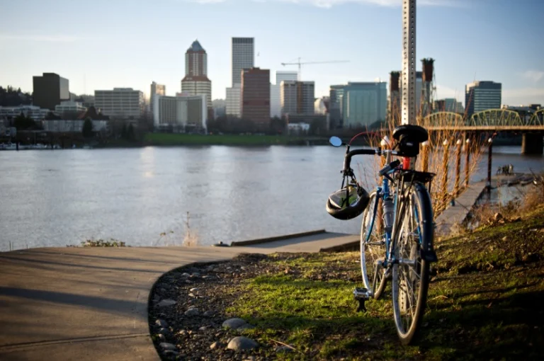 Fiets met helm geparkeerd langs een fietspad aan de oever van de Willamette rivier met de skyline van Portland en een brug op de achtergrond