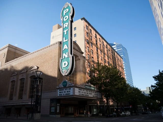 Verticale neonreclame met de tekst Portland aan de gevel van een historisch theatergebouw in het centrum van de stad