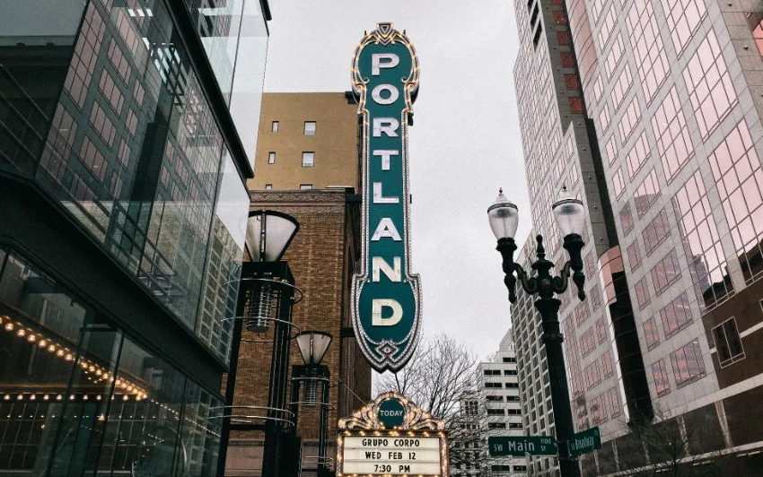 Verticaal neonbord met de tekst Portland hangt aan een theatergevel tussen straatlantaarns in het centrum van Portland