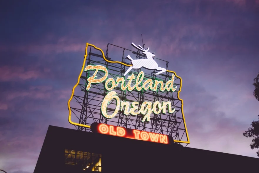 Verlicht neonbord met de tekst Portland Oregon Old Town en een springend hert erboven kleurt de avondlucht