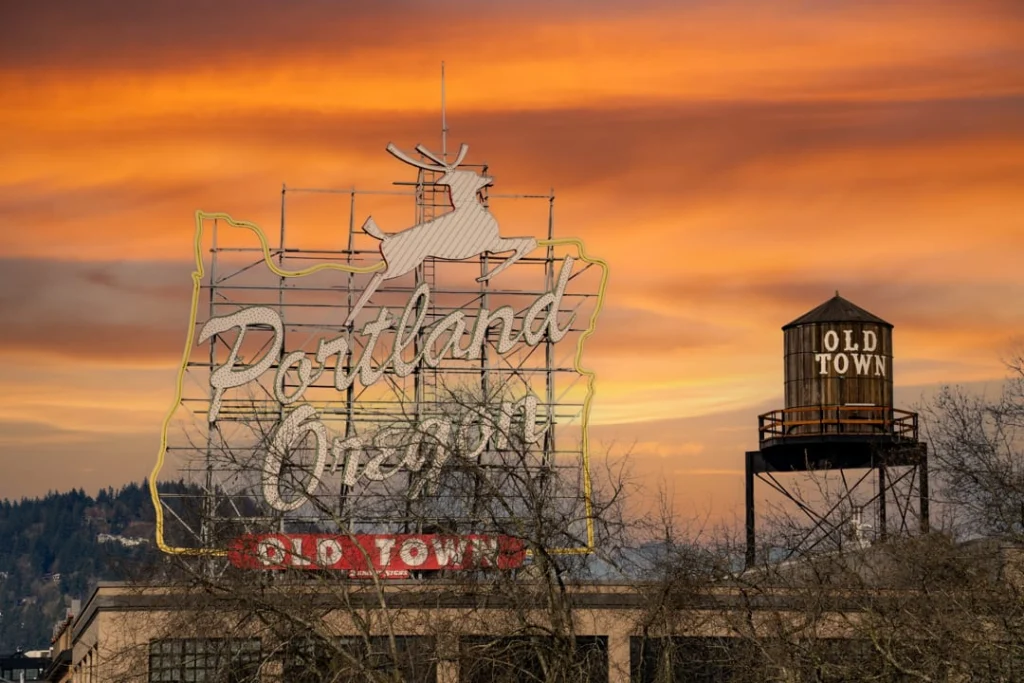 Verlicht neonbord met de tekst Portland Oregon en een springend hert, naast een watertoren met het opschrift Old Town