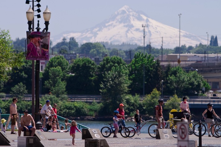 Mensen fietsen en spelen langs de waterkant in Portland terwijl de besneeuwde Mount Hood oprijst boven de stad
