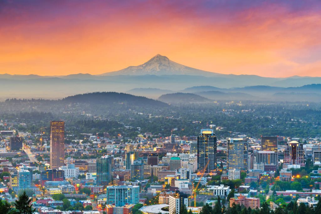 Verlichte skyline van Portland in de avondschemering met de besneeuwde top van Mount Hood boven de heuvels op de achtergrond