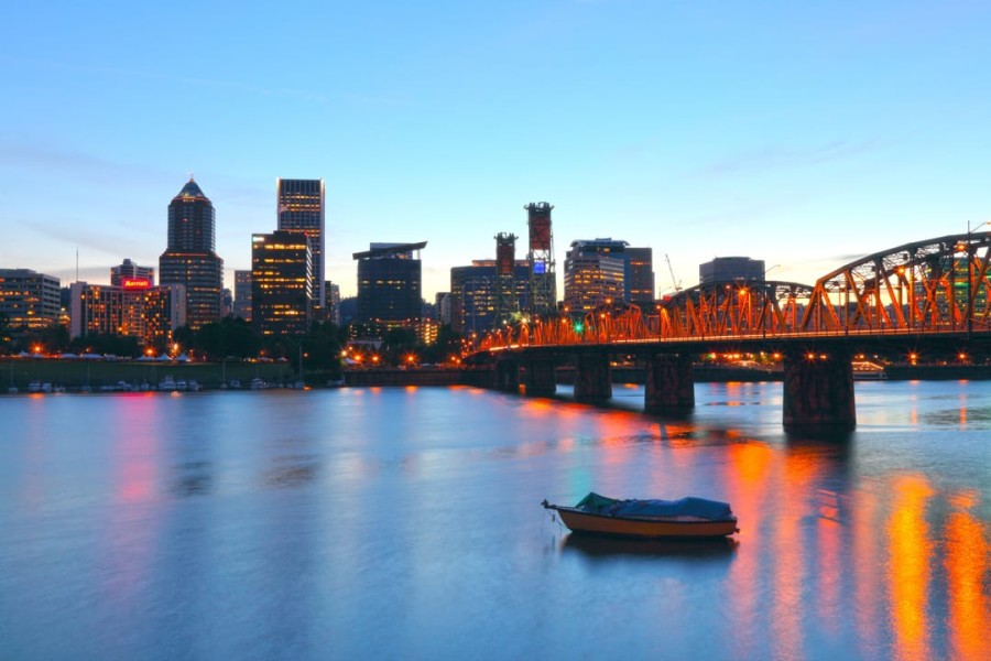 Verlichte skyline van Portland met een oranje brug over de rivier en een klein bootje op het water tijdens de schemering