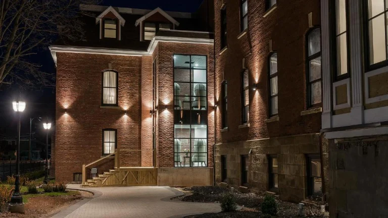 Gerenoveerd bakstenen gebouw met grote glazen pui, verlichte gevel en trap naar de ingang, gefotografeerd in de avond op Prince Edward Island