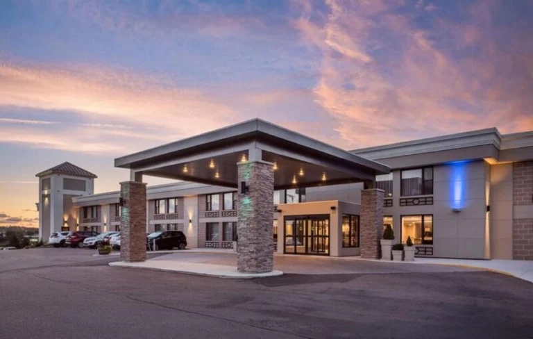 Modern hotelgebouw met een grote overkapping bij de ingang en geparkeerde auto's, gefotografeerd bij een roze en paarse avondlucht op Prince Edward Island