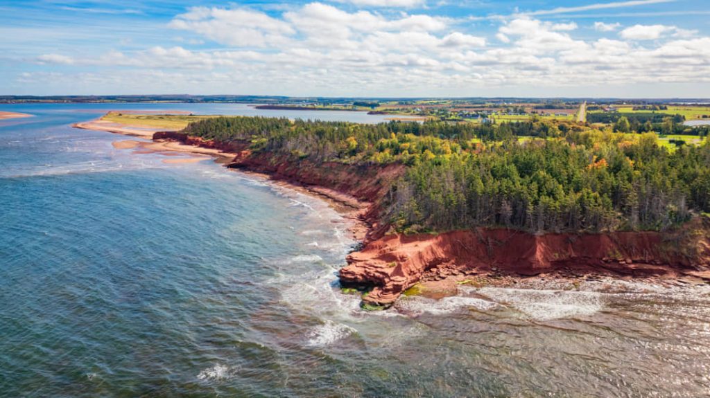 Luchtfoto van rode zandstenen kliffen begroeid met bos die overgaan in een strand en de zee op Prince Edward Island