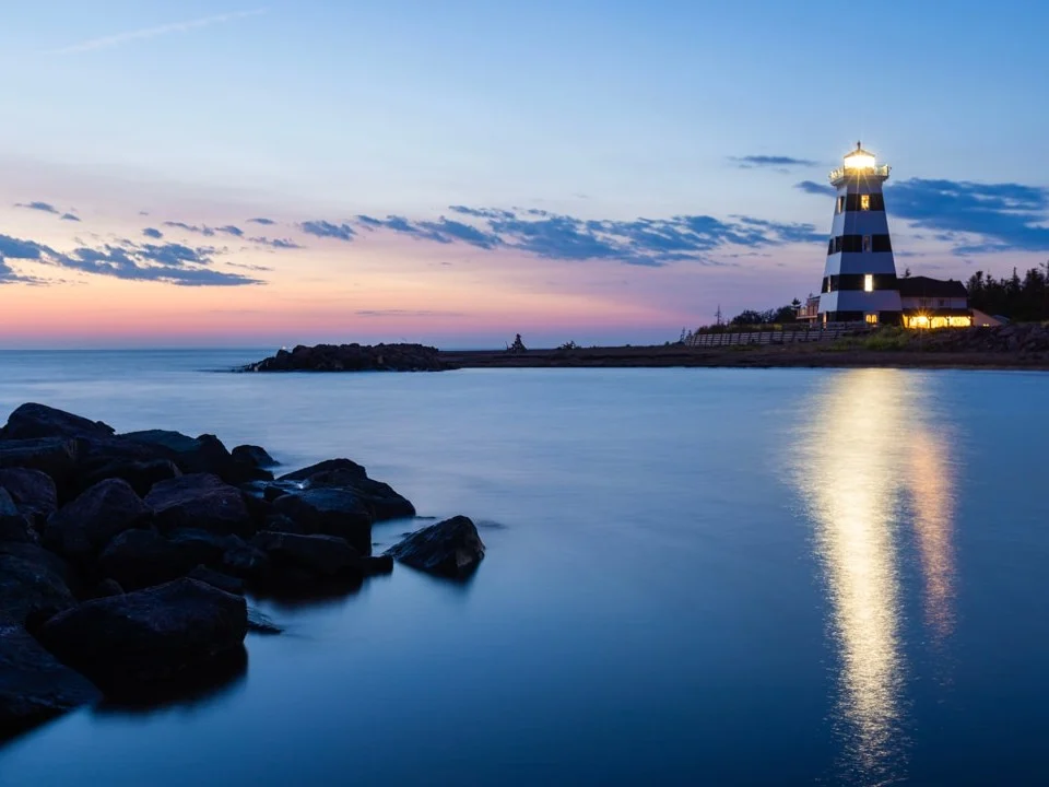 Zwart witte vuurtoren met brandend licht aan het water op Prince Edward Island weerspiegeld tijdens de schemering