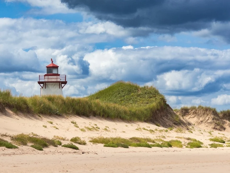 Kleine rood witte vuurtoren bovenop een begroeide zandduin met een dreigende bewolkte lucht op de kust van Prince Edward Island
