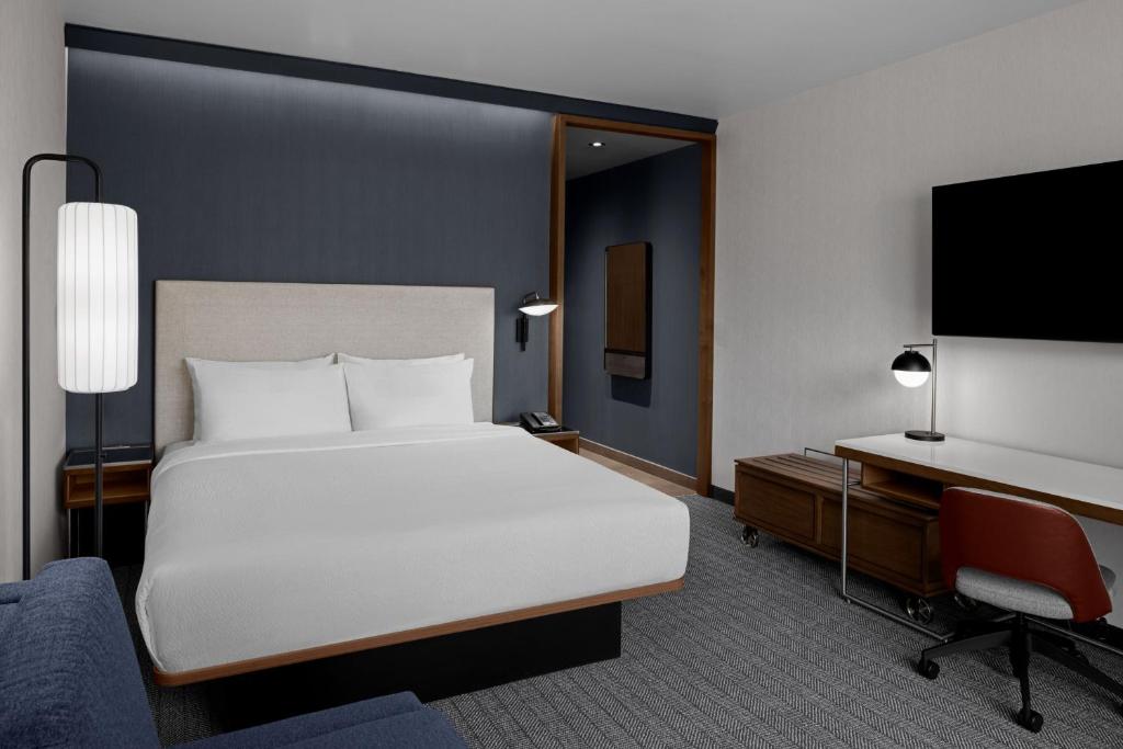 Moderne hotelkamer met een bed tegen een donkerblauwe wand, een bureau met stoel en een grote televisie