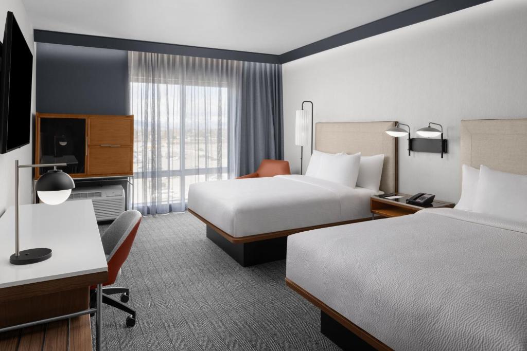 Hotelkamer met twee bedden met houten frame, een oranje stoel en een bureau bij het raam