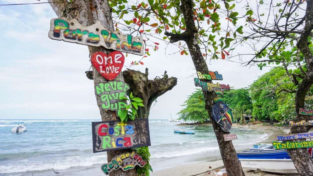 Handgeschilderde houten bordjes met teksten als Costa Rica en One Love hangen aan een boom op het strand van Puerto Viejo de Talamanca